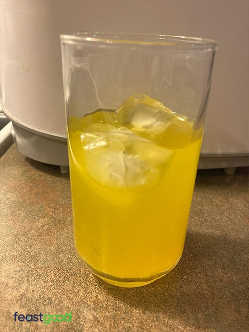 TL Creatine HMB Creatine Supplement Peach Rings - FeastGood.com Tall clear glass of yellow-orange juice with ice cubes on a kitchen countertop.